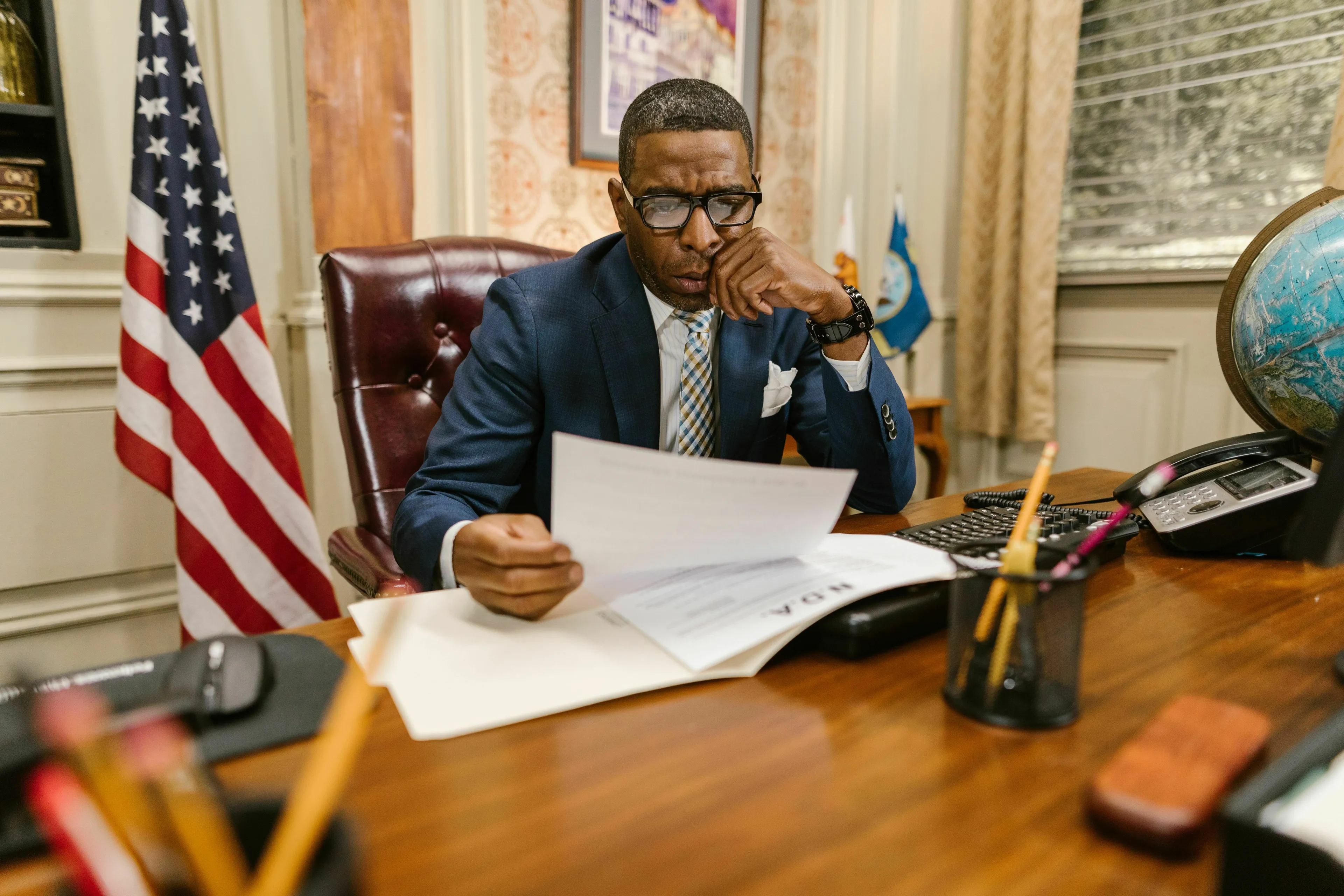 A man sitting at a desk, looking intently at a document, representing the question about the first President of the United States.