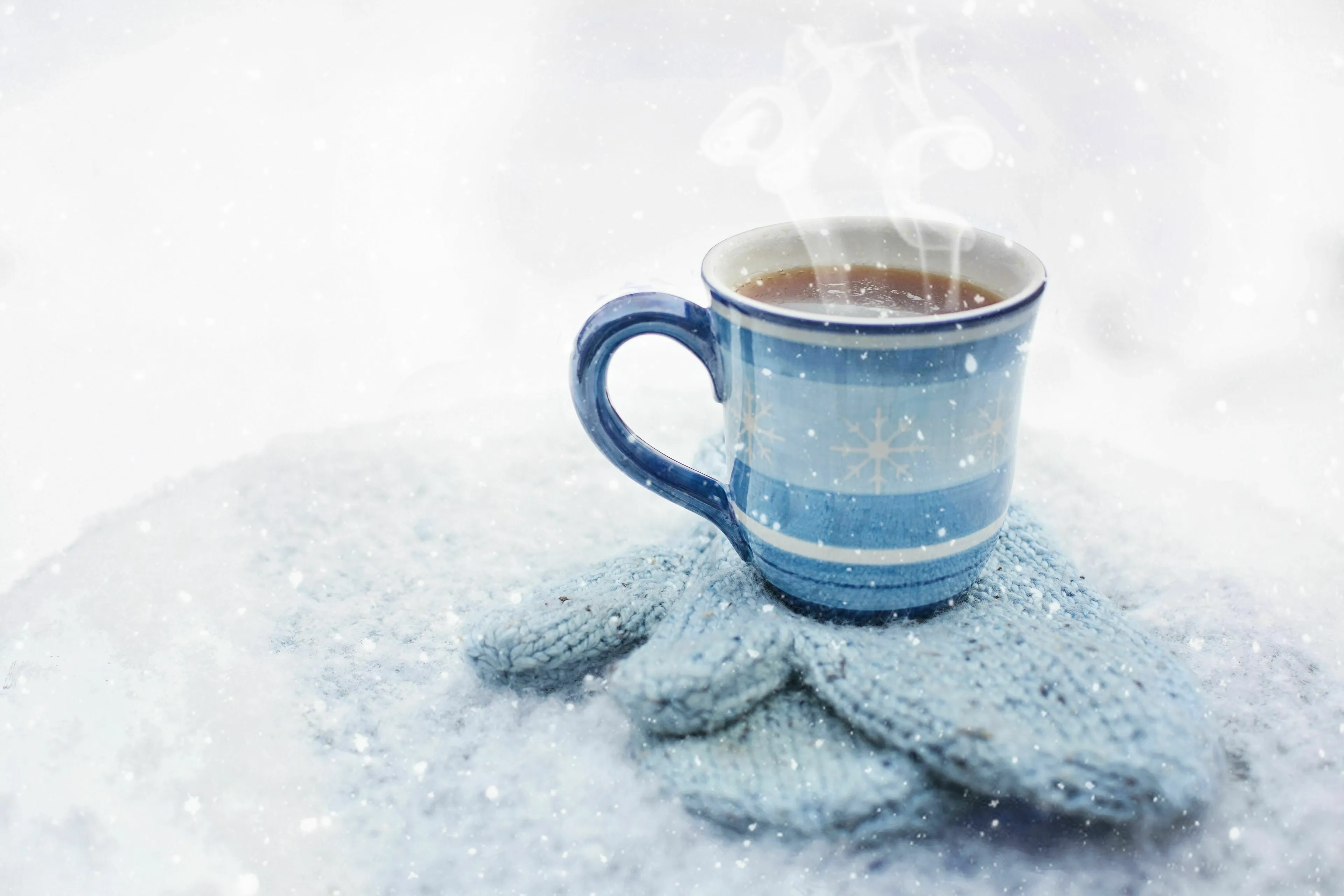 A steaming mug on a knitted glove in a snowy landscape, illustrating water turning into water vapor.