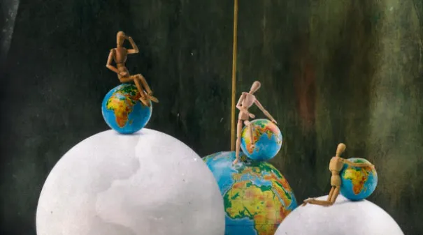 Three wooden figures on different globes, representing the force of gravity for science school questions.