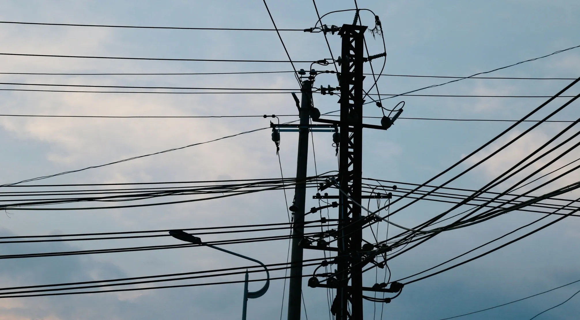 Silhouette of utility poles with numerous electrical charges wires against a cloudy sky. Which device stores electrical charges?
