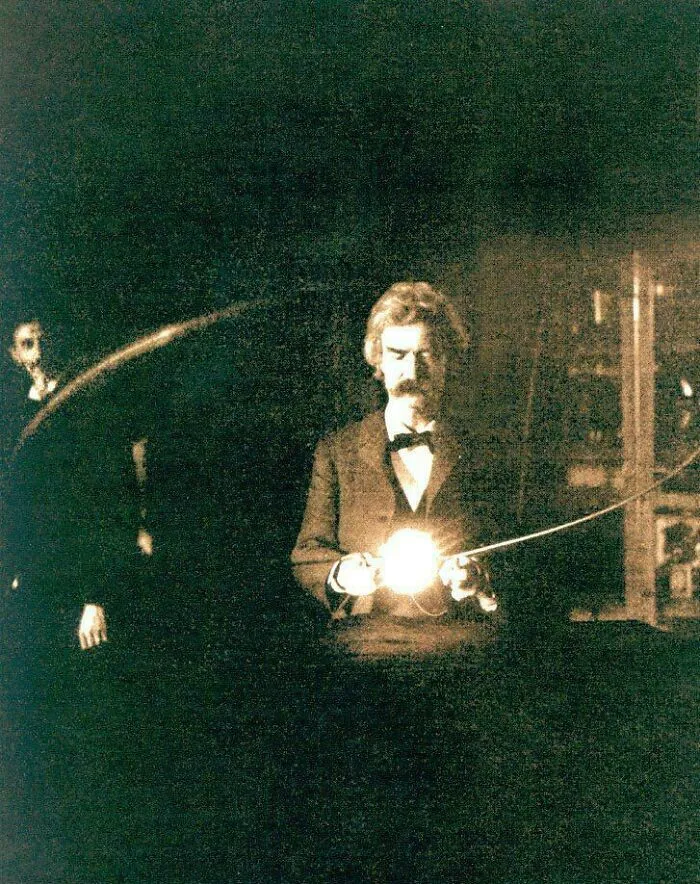 Mark Twain Holding A Lamp Lit Without A Wired Connection In Nikola Tesla's Laboratory While Tesla Watches From The Shadows, 1894