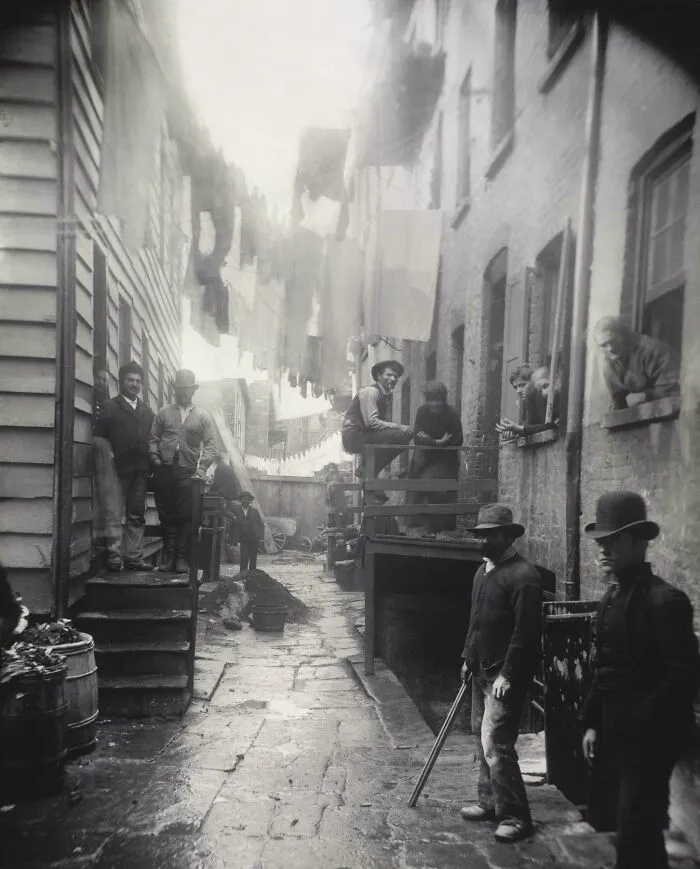 Heartbreaking photo from history of an alleyway with laundry hanging overhead, people standing around, and brick buildings