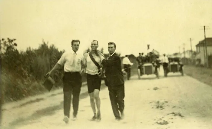 A beautiful historical photo showing an exhausted runner being supported by two men during an old marathon race.