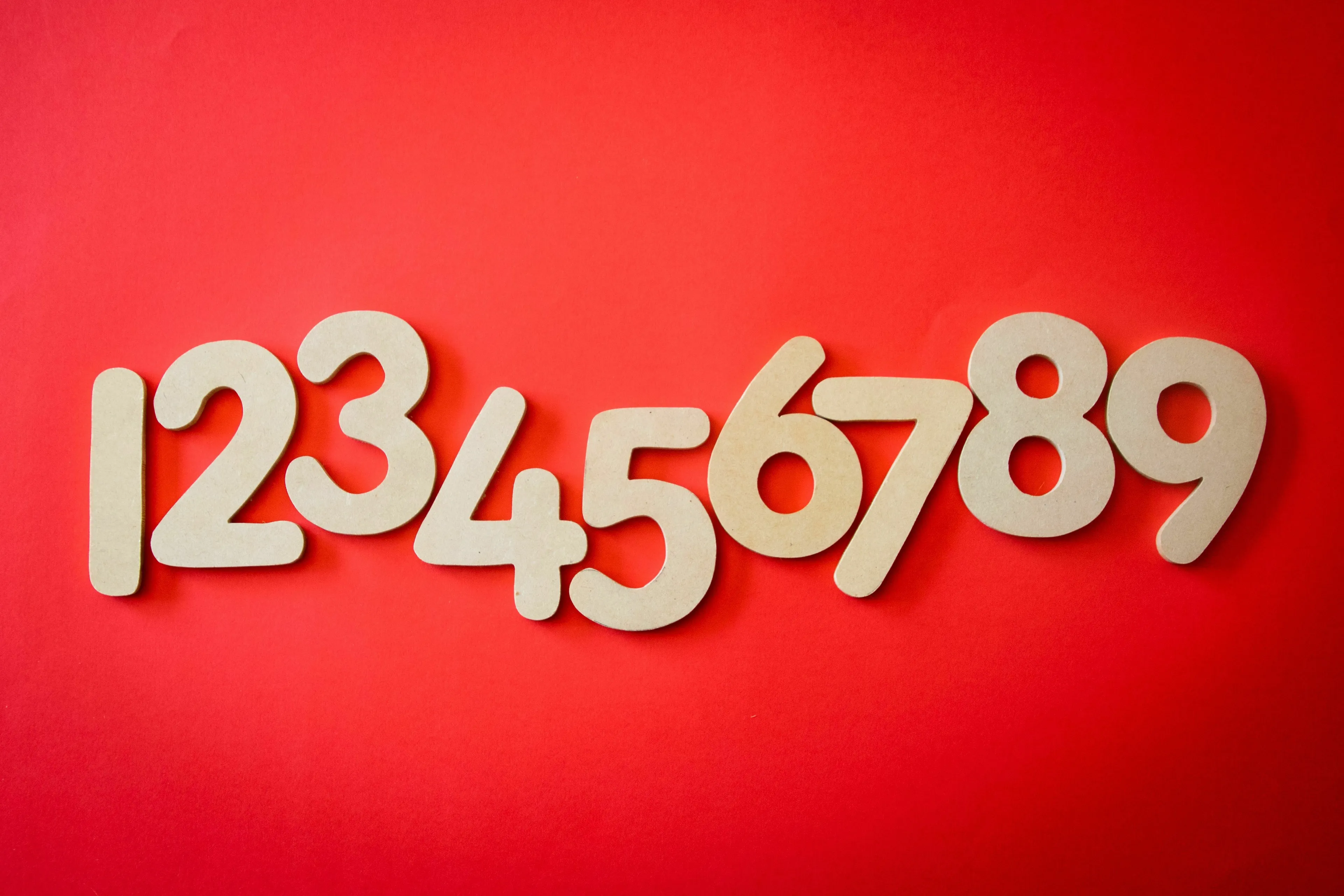 Wooden numbers 1 through 9 arranged in a line on a red background, used for a One Percent Club Test question about alphabetical order.