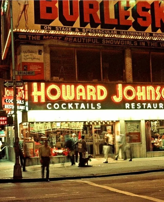 A fascinating photo from American history of a lively street scene at night, featuring a Howard Johnson restaurant and a Burlesque sign.