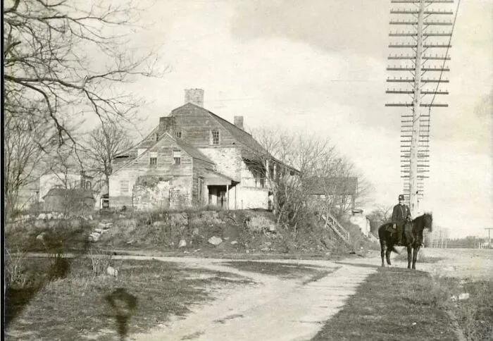 A man on horseback near an old house and telephone poles, a rare photo from American history.