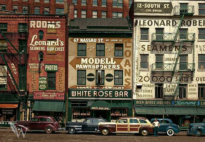 A colorful street scene with vintage cars parked in front of various shops, a fascinating photo from American history.