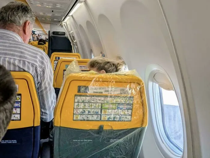A passenger on an airplane with their head stuck through the seat, highlighting little hope for humanity.