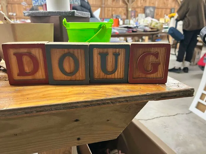 Four wooden blocks spelling out the name DOUG, sitting on a rustic wooden table amidst other items. A sign from the universe.