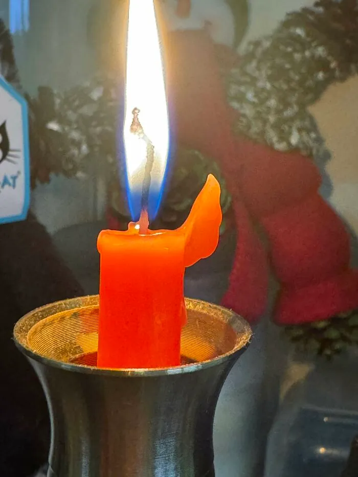 A lit orange candle with a bright flame, melting into a unique, wing-like shape. A sign from the universe.