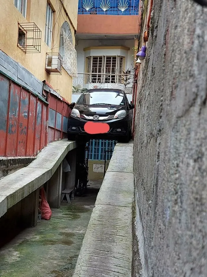 A black car precariously stuck between two narrow concrete ramps, illustrating people so dumb.