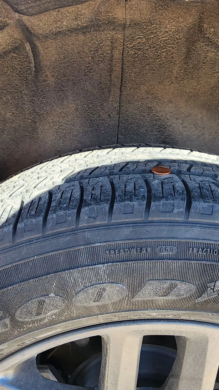 A car tire with a penny stuck in the tread, showcasing a dumb moment of misfortune.