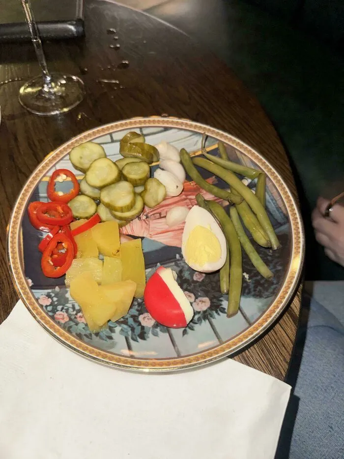 A plate holding sliced pickles, peppers, cheese, and a hard-boiled egg as questionable food combos.