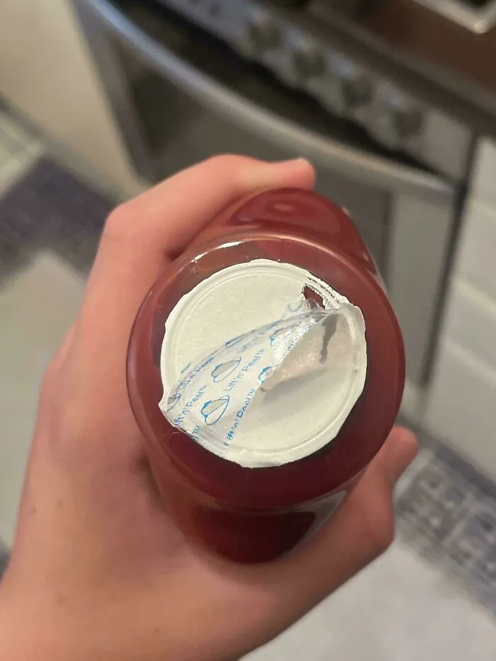 A hand holding a bottle with an incorrectly peeled bottle seal.
