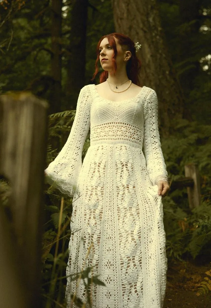 Woman wearing a white crochet dress standing in wooded area
