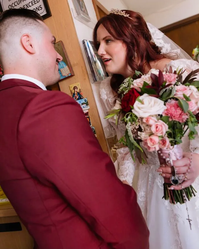 A bride in a white dress and veil with a bouquet looks up at her groom in a funny wedding photo.