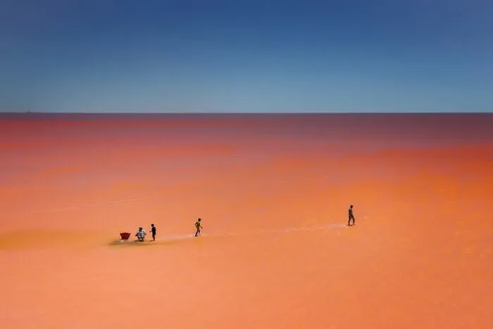 Murat Bakmaz captures the beauty of everyday life, people on an expansive, reddish-orange landscape under a blue sky.