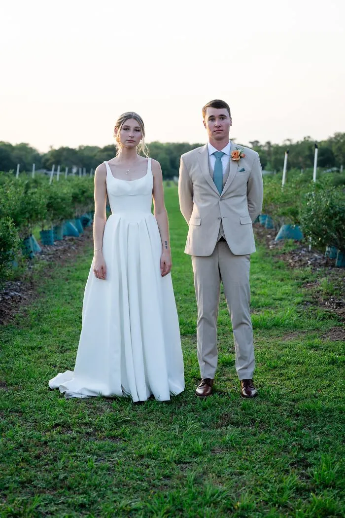 An iconic wedding photo of a stoic bride and groom standing in a lush green field of blueberry bushes.