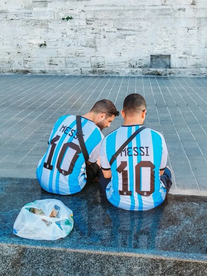 Two men in Messi #10 jerseys sitting on steps, an example of well-timed street shots.