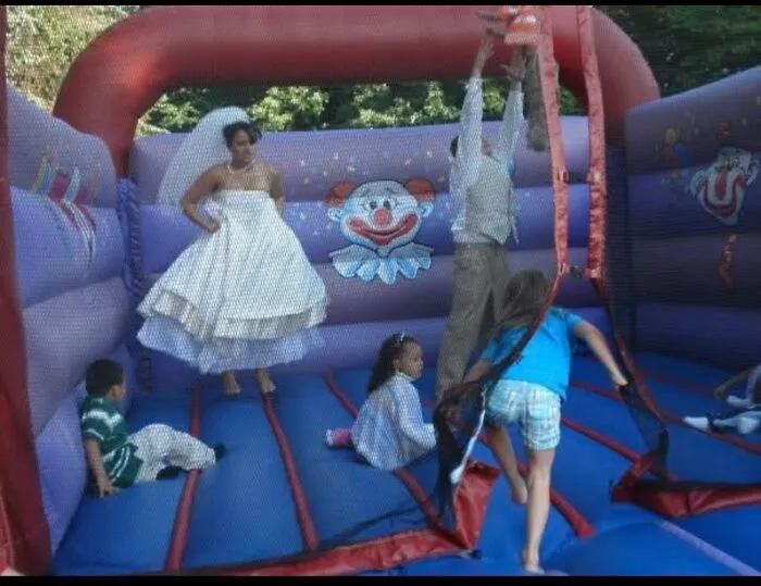 Bride on a bouncy castle, with kids and groom, enjoying funny wedding photos.