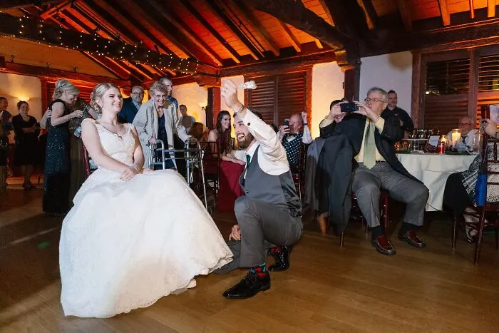 Groom takes off the garter from the bride, seated, making for funny wedding photos.