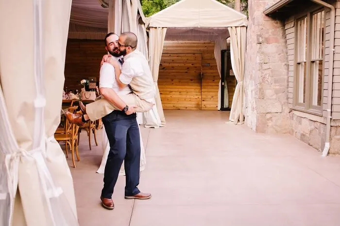 Funny wedding photos: Groom carrying his husband, sharing a kiss, in a playful and iconic moment.