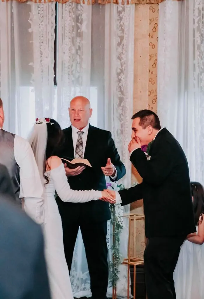 Funny wedding photos: Groom laughing and wiping tears while holding hands with the bride during the ceremony.