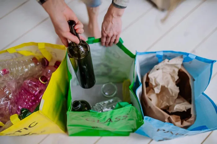 A person sorting glass, plastic, and paper into separate bins, highlighting dumb work rules about recycling.