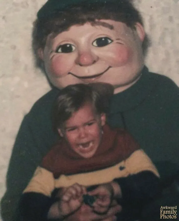 Awkward family photos: A crying child sits on the lap of a terrifying character mascot with rosy cheeks.