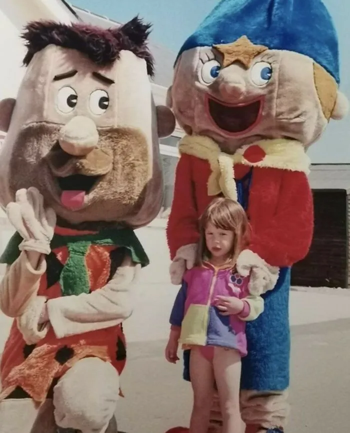 Awkward family photos: A little girl stands between two terrifying character mascots resembling cartoon characters.