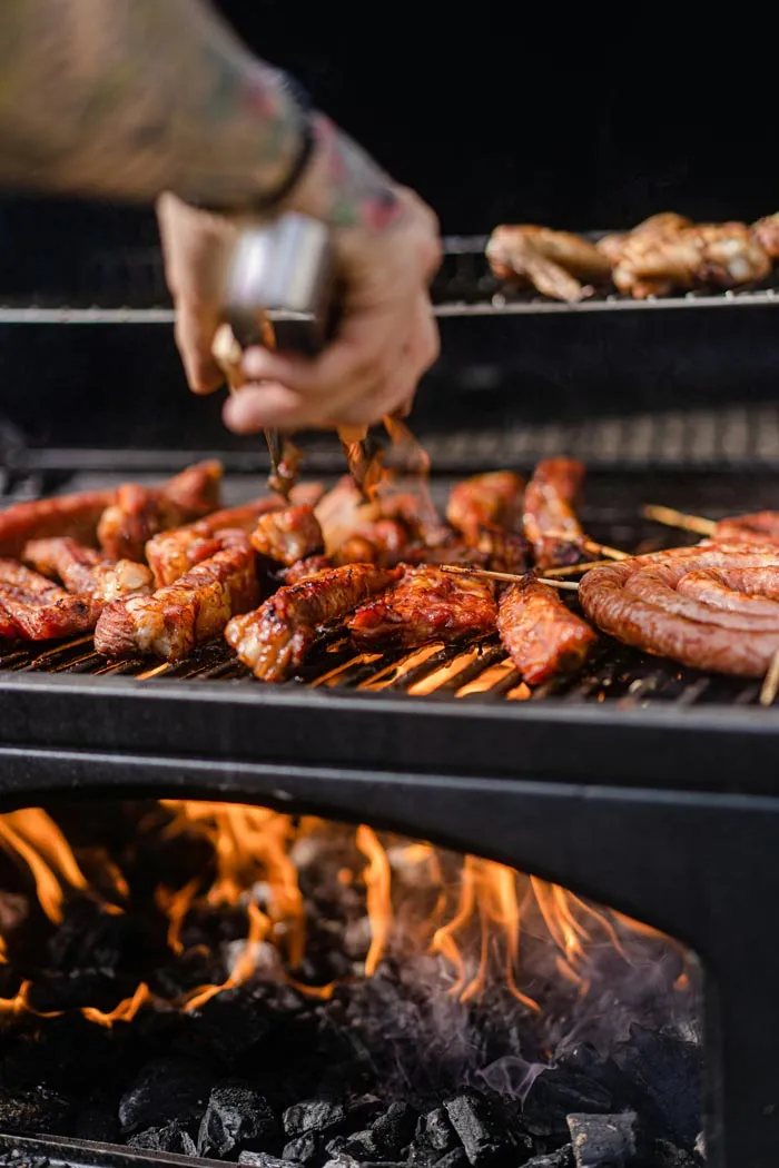 A hand using tongs to turn various meats on a hot grill with visible flames, related to dumb work rules.