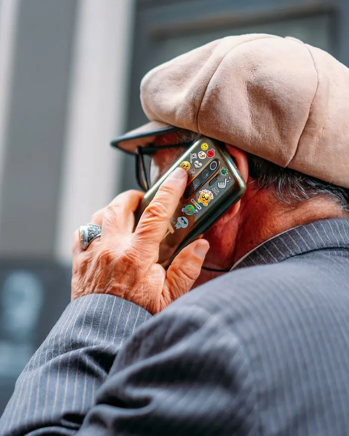 A photographer captured a well-timed street shot of an older man talking on a sticker-covered phone.