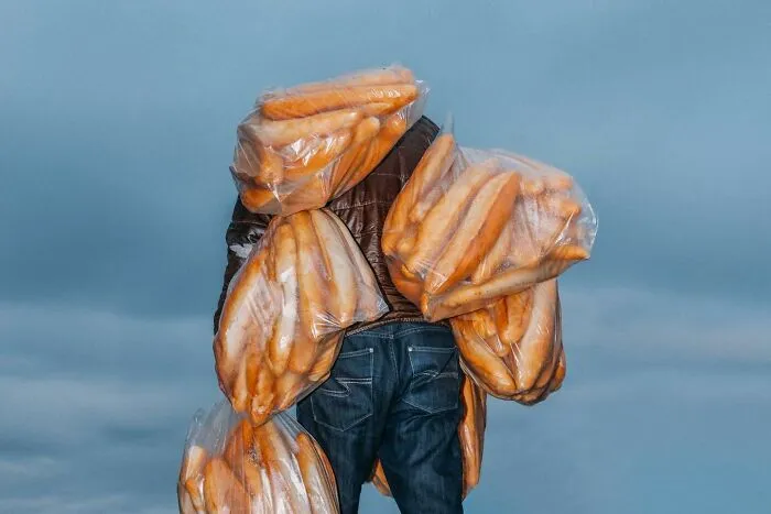 A photographer captured well-timed street shots of a person carrying multiple bags of bread against a light blue sky.