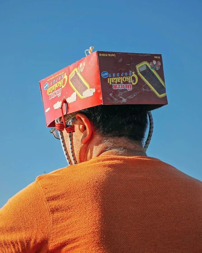 A man wearing a box as a hat in a well-timed street shot.