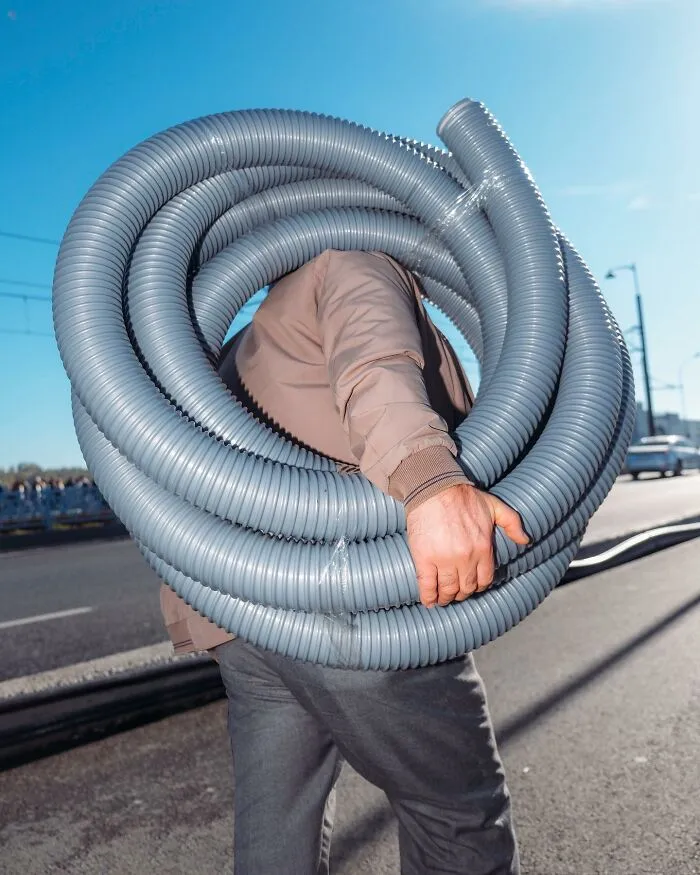 A photographer captured a ridiculously well-timed street shot of a man carrying a large roll of gray tubing.