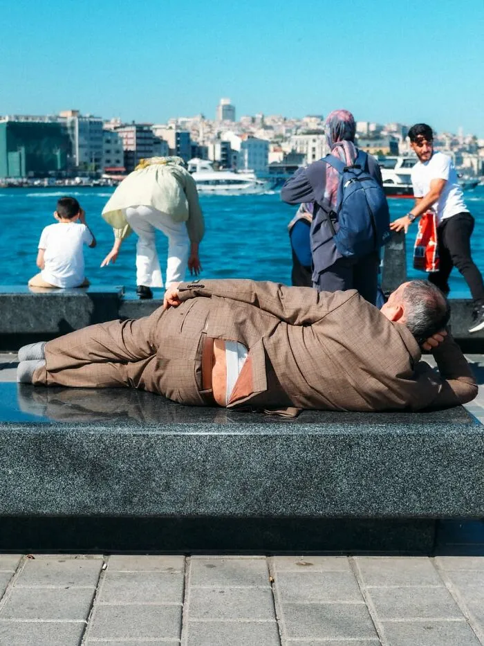 A man in a suit lying on a bench with his underwear showing, a candid moment in well-timed street shots.
