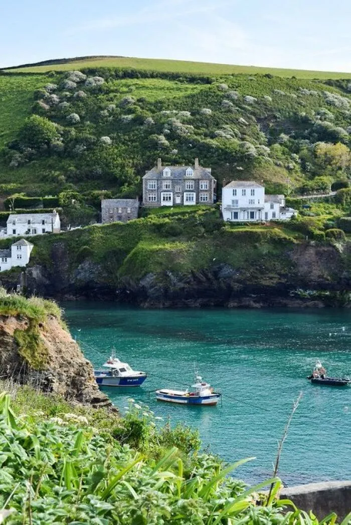 Coastal buildings with so much character overlooking a turquoise bay with boats, surrounded by lush green hills.
