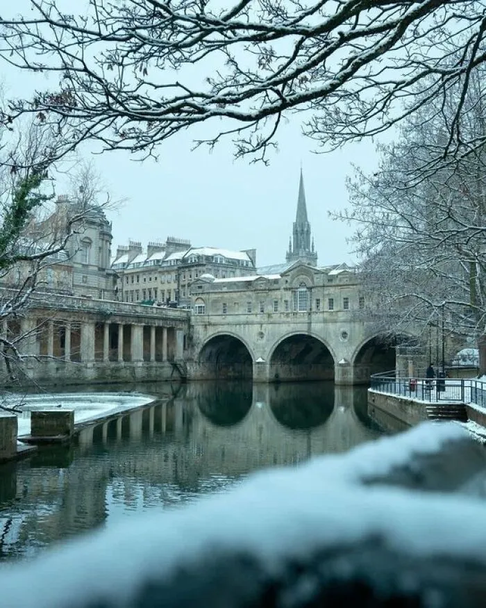 A snowy winter landscape featuring a historic bridge over a river, exemplifying buildings with so much character.