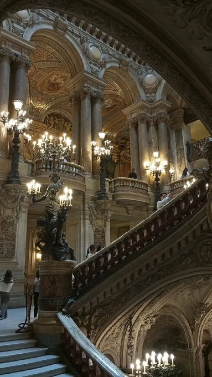 Grand interior of a historic building with character, showcasing ornate staircases, chandeliers, and classical columns.