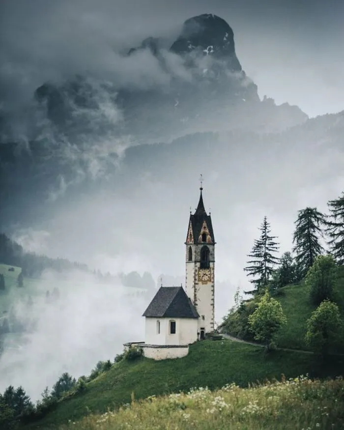 A charming old church on a misty mountainside, highlighting buildings with character in a dramatic landscape.