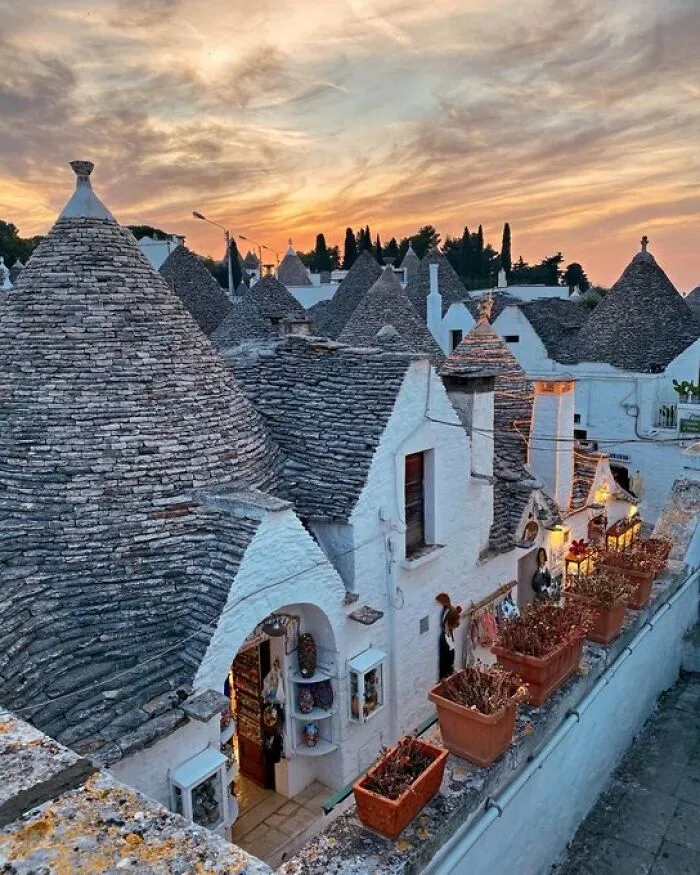 Quaint white buildings with conical roofs and warm lights glow under a vibrant sunset, showcasing charming architectural character.