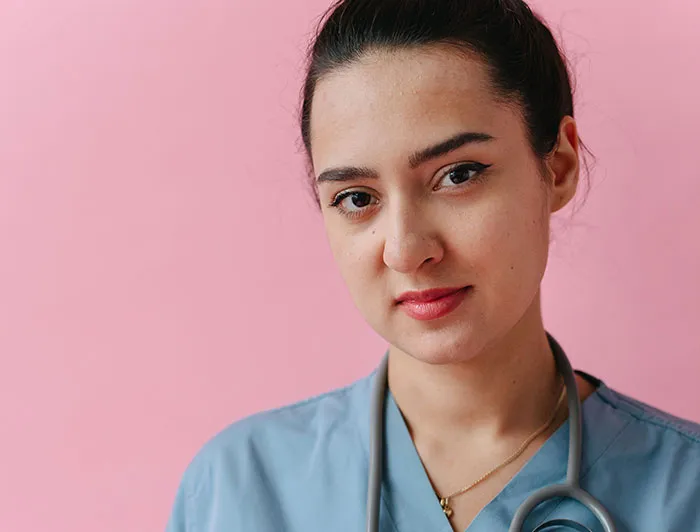 A nurse in blue scrubs with a stethoscope, looking at the camera, conveying patients said weird things.