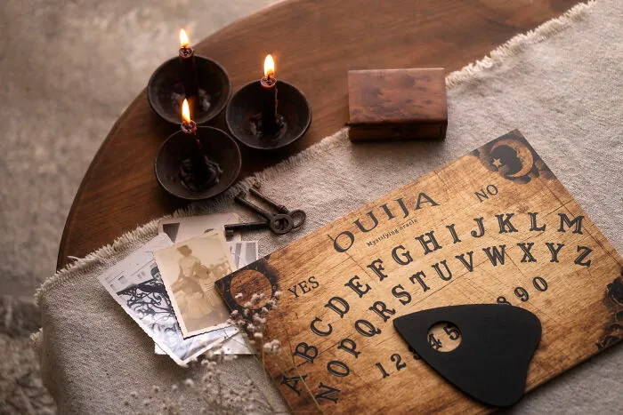An ouija board, lit candles, old photos, and keys on a table, symbolizing a sign from the universe and spiritual connection.
