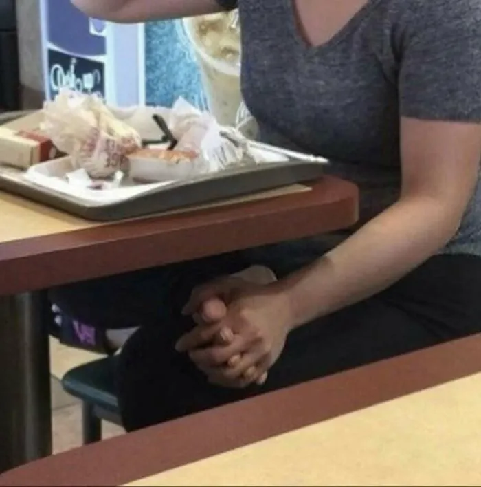 A person with an extra pair of hands folded together at a table, a random and unhinged image.