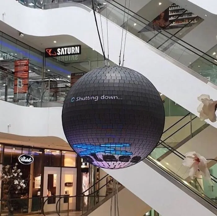 A large disco ball hanging in a mall, displaying a shutdown message, presenting a cursed and unhinged scene.