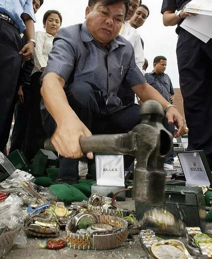 A man smashing replica Rolex watches with a hammer, a random and unhinged moment.