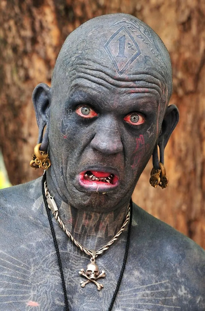 Man with extensive tattoos, stretched earlobes, and red eyes, an amazing world record throughout history.