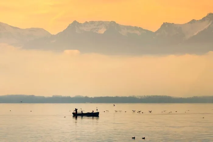 Murat Bakmaz captures the beauty of everyday life with a boat on a misty lake against mountains at sunset.