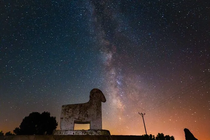 Murat Bakmaz captures the beauty of everyday life: A stone ram statue under a vibrant Milky Way at night.