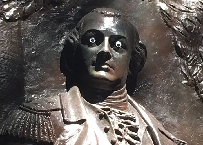 Unsettling picture of a historical bronze bust with googly eyes affixed to it, creating a humorous yet bizarre effect.